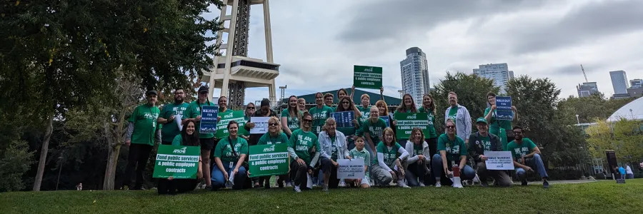 Photo of WFSE members in green shirts holding signs that say "Fund public services and public employee contracts"
