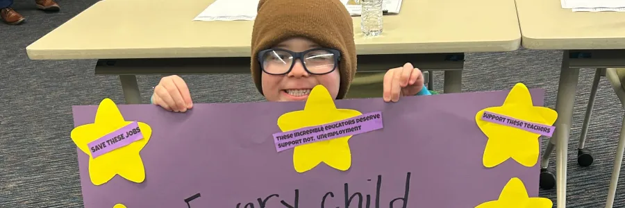 A child holds a sign reading "Every child shines brighter because of them!"