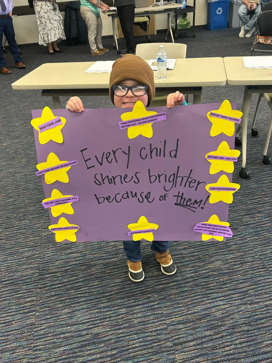 A child holds a sign reading "Every child shines brighter because of them!"