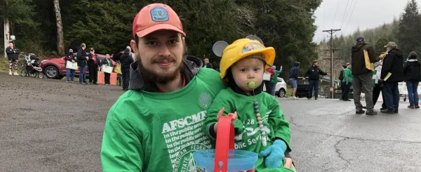 Photo of man in AFSCME green shirt holding an infant in a green shirt